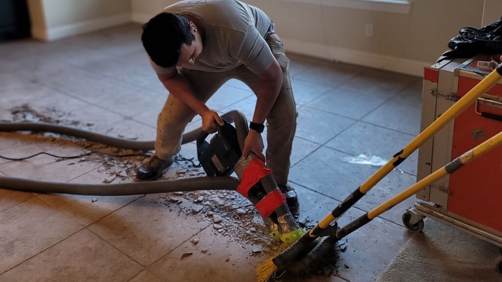 a worker using a floor scraper to remove tiles from a concrete floor during a tile removal project