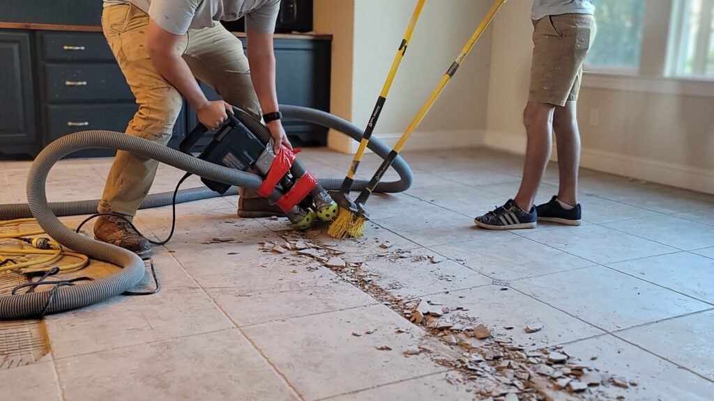 A worker using a tool to remove tiles from a floor