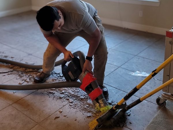 a worker using a floor scraper to remove tiles from a concrete floor during a tile removal project